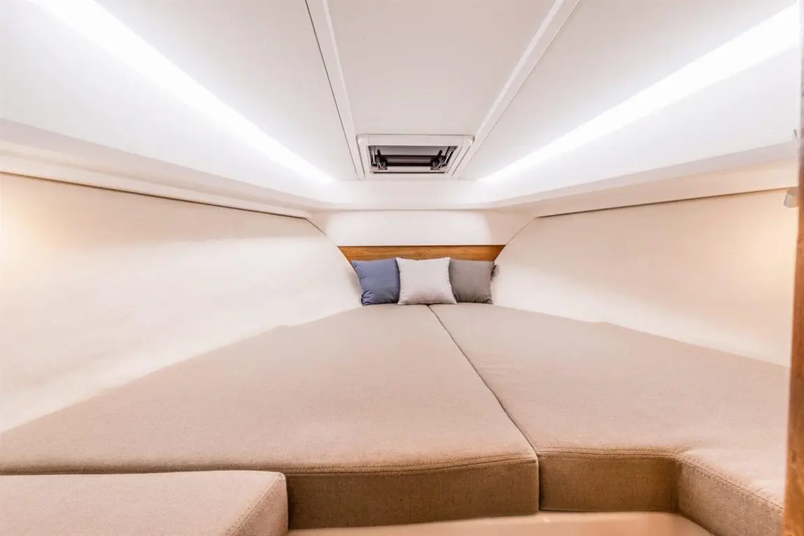 Spacious cabin interior featuring a large bed, soft beige bedding, and decorative cushions against smooth white walls.